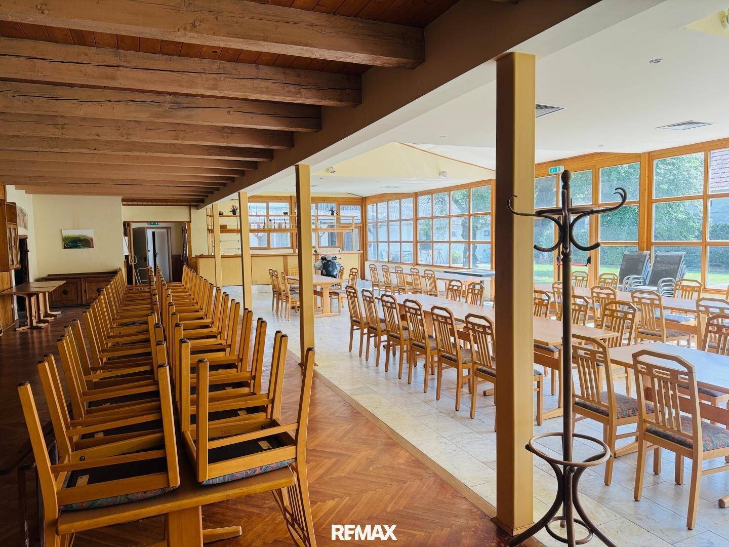 Großer, heller Speisesaal mit vielen Tischen und Stühlen, umgeben von großen Fenstern.