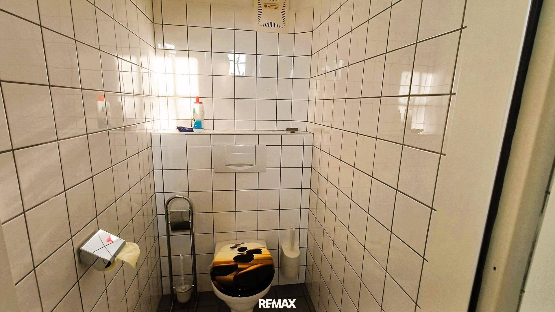 Kleiner Toilettenraum mit weißen Fliesen an Wänden und Boden, ausgestattet mit WC und Lüfter.