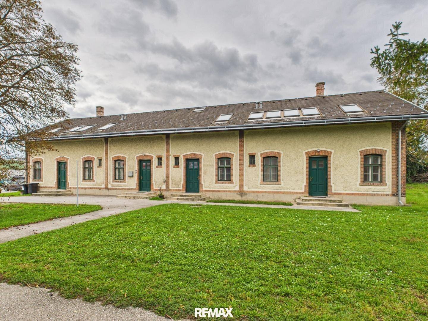 Historisches Gebäude mit mehreren Eingängen und Dachfenstern, umgeben von einer grünen Rasenfläche.