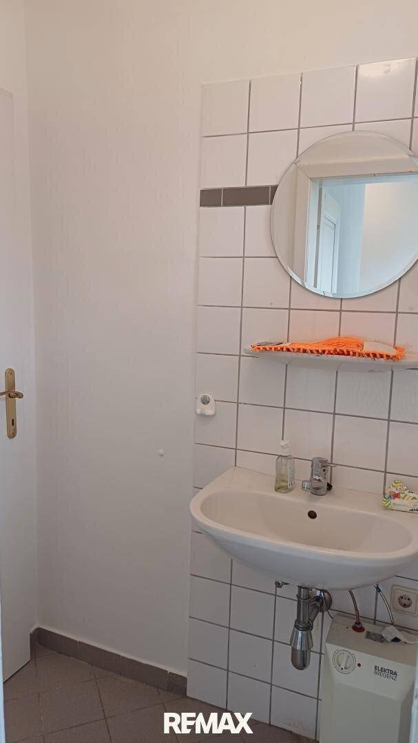 Badezimmer mit weiß gefliesten Wänden, einem Waschbecken und einem runden Spiegel über einem Regal.