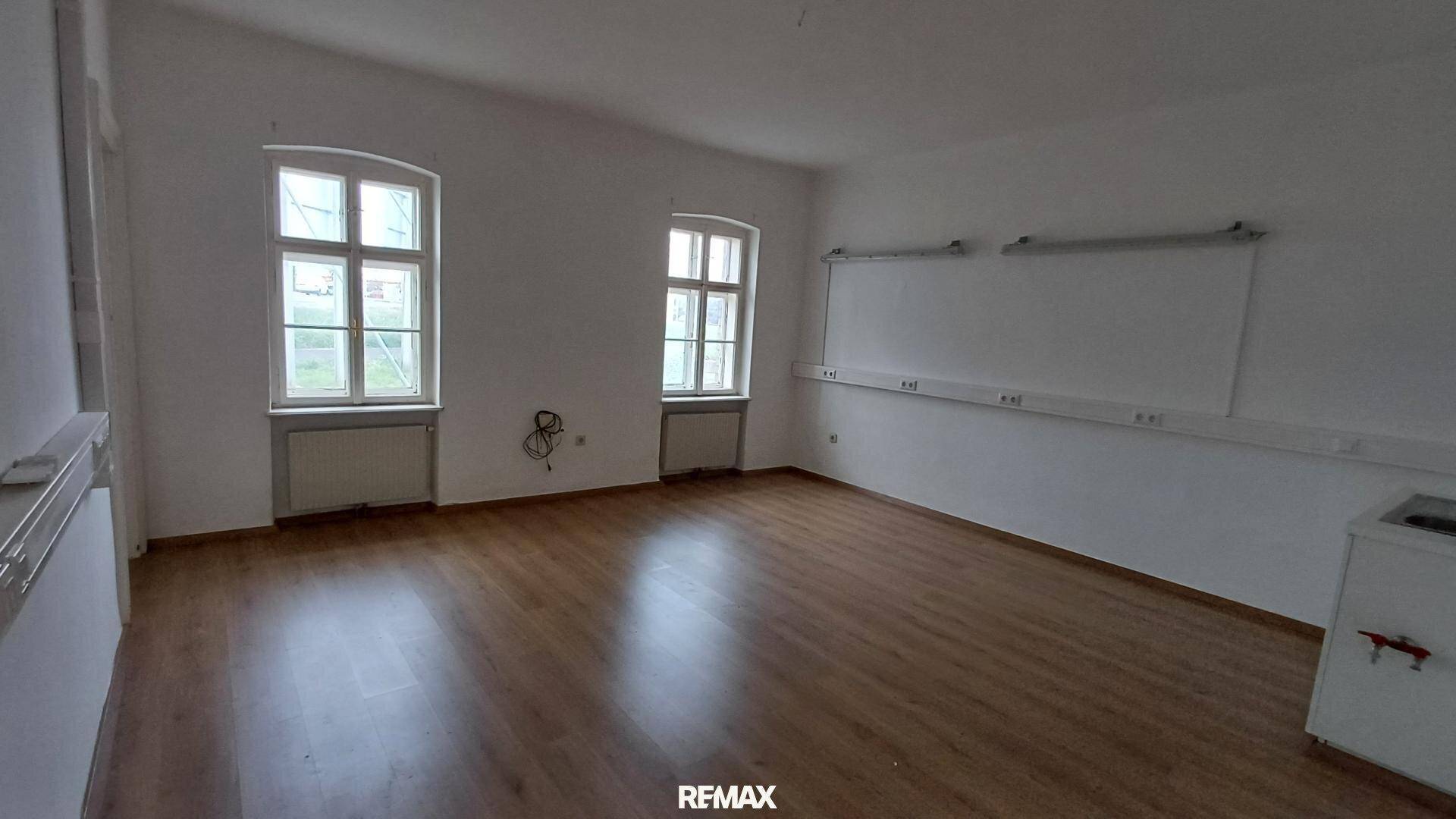 Heller und geräumiger Büroraum mit zwei Fenstern, Laminatboden und Whiteboards an den Wänden.