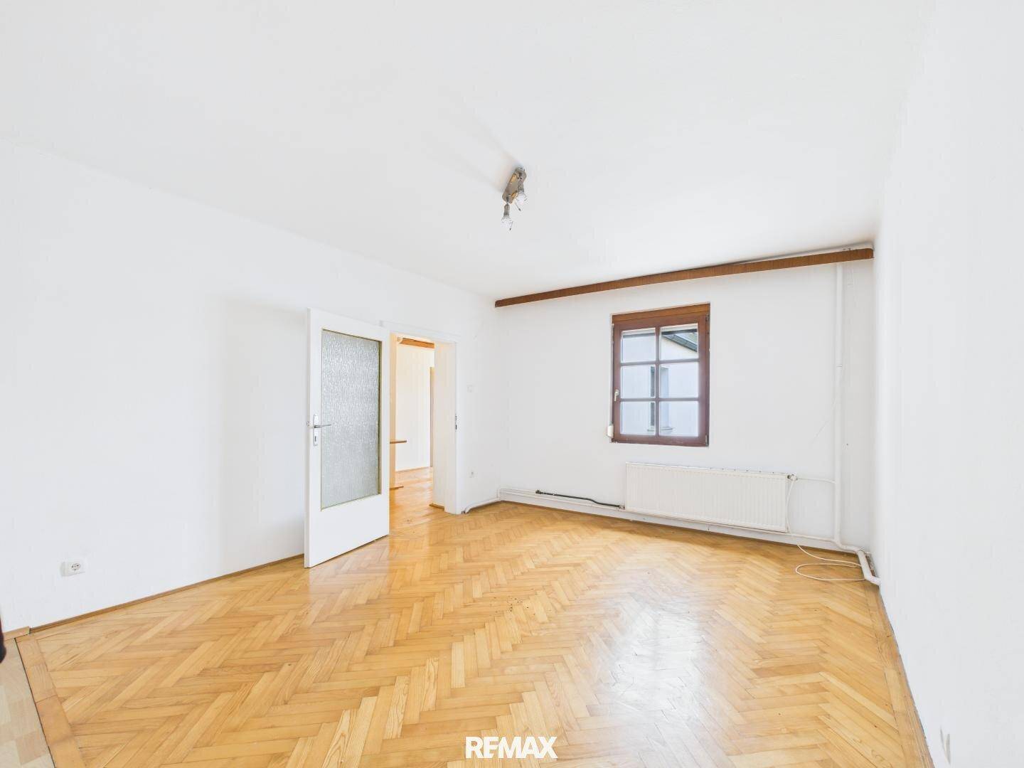 Helles Zimmer mit Fischgrätparkettboden und einem Fenster, das viel Tageslicht hereinlässt.