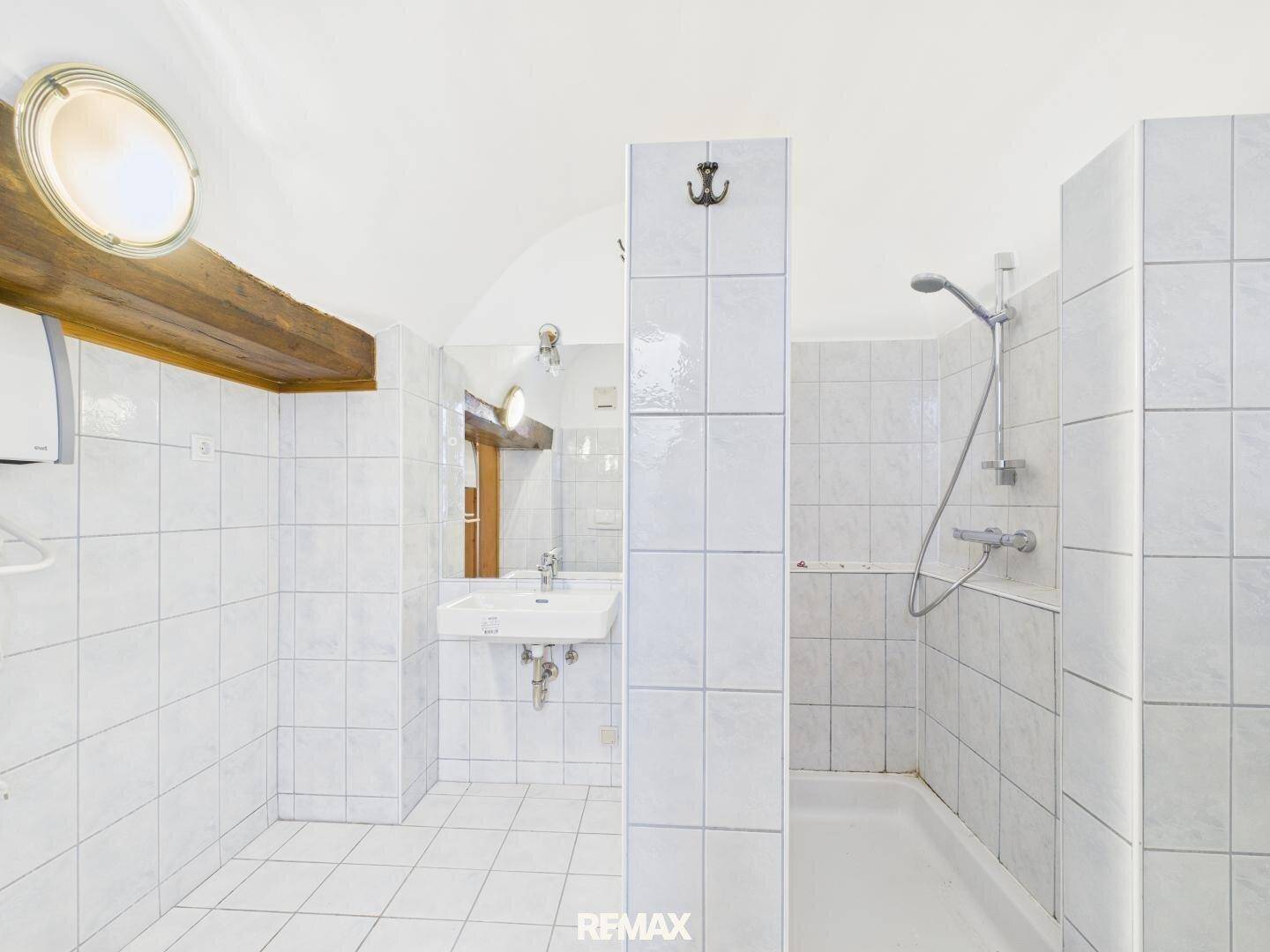 Funktionales Badezimmer mit weißen Fliesen, Dusche und Einzelwaschbecken.
