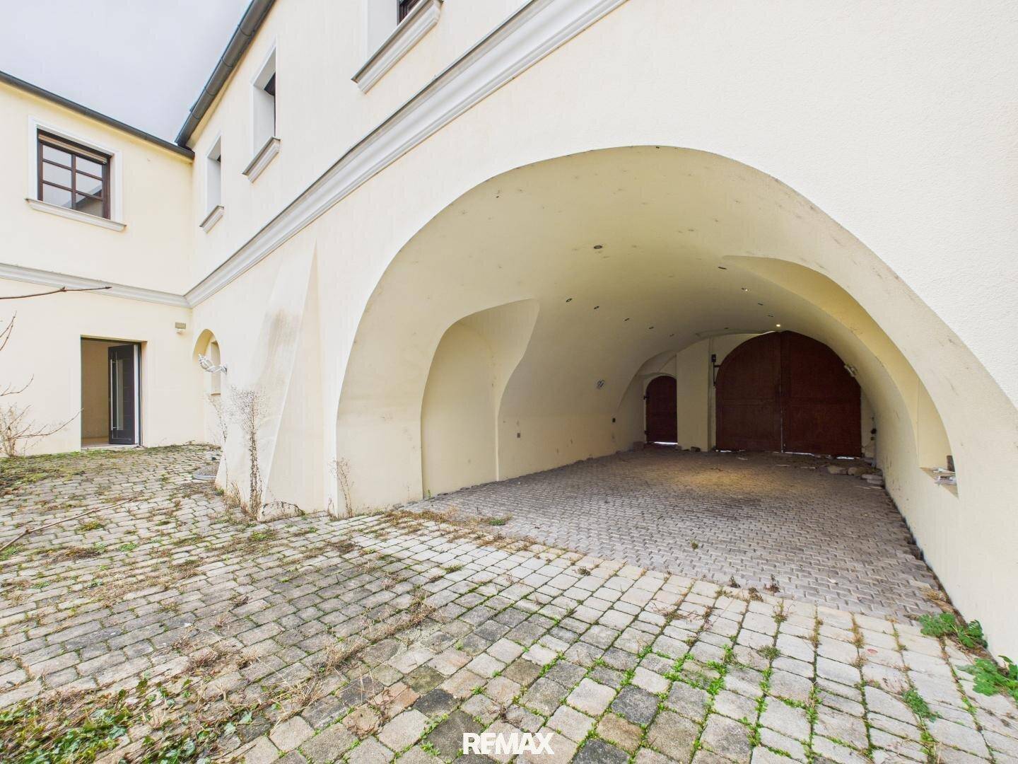 Gepflasterter Innenhof mit großem Torbogen, der zu einem überdachten Garagenbereich führt.