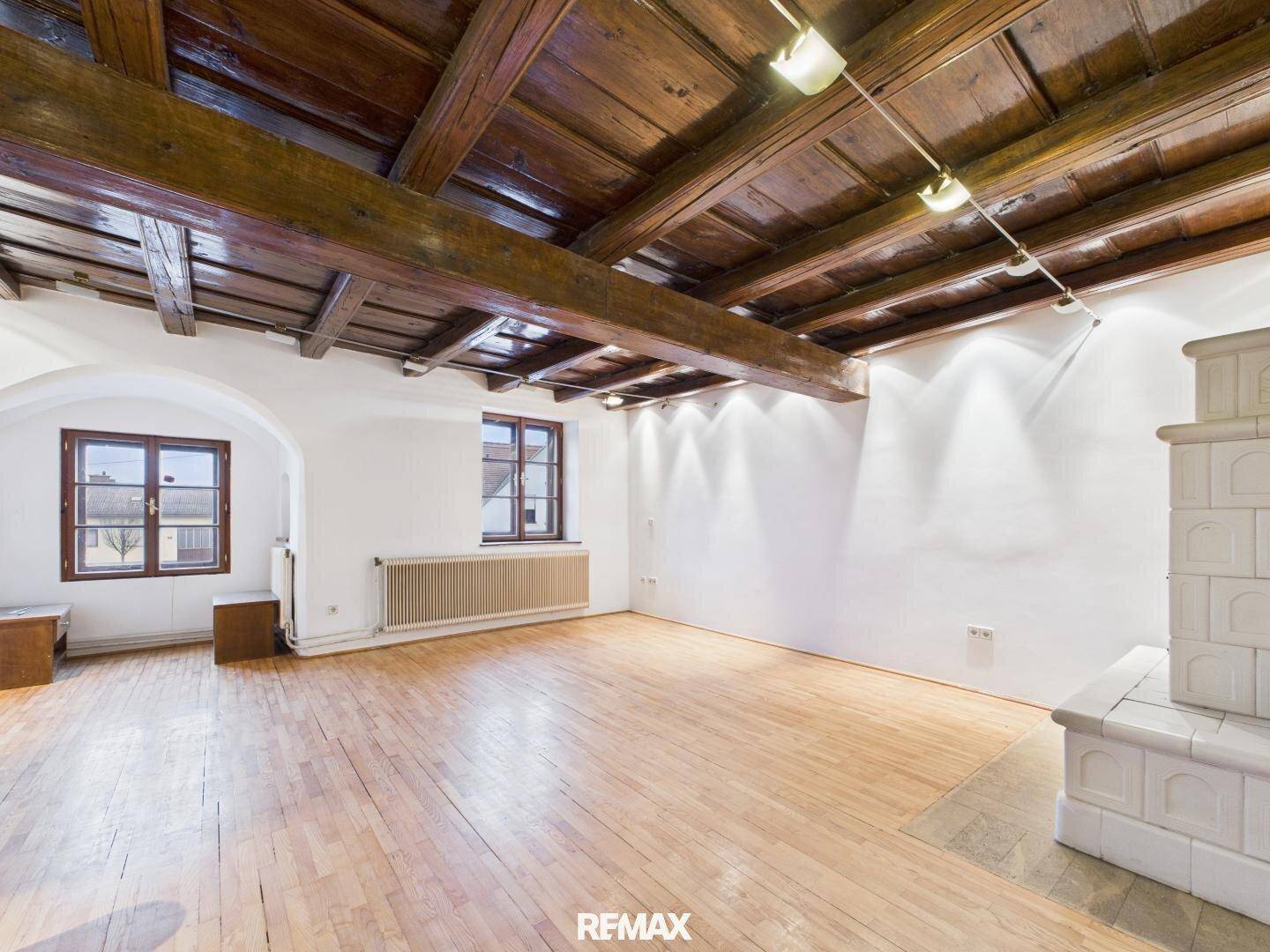 Großes Wohnzimmer mit Holzboden, sichtbaren Deckenbalken und traditionellem Kachelofen.