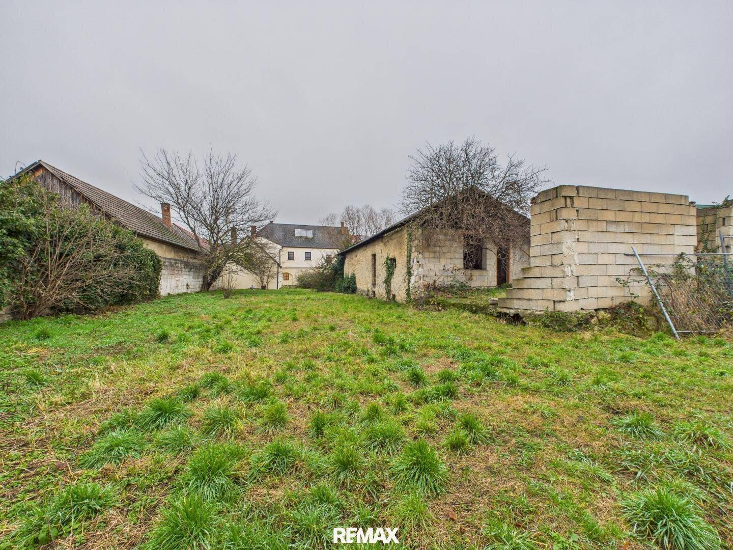 Weitläufige Grünfläche mit alten Nebengebäuden im Hintergrund, ideal für Gartengestaltung.