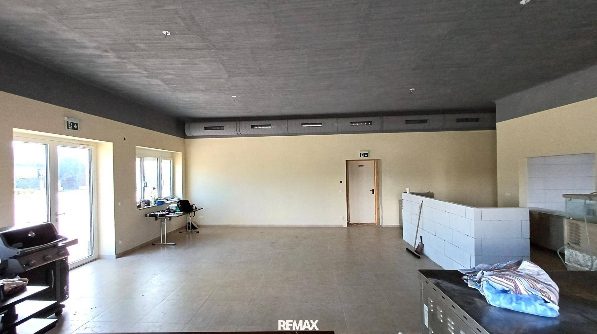 Großer, leerer Gewerberaum mit Fliesenboden, hohen Decken und Zugang nach draußen.