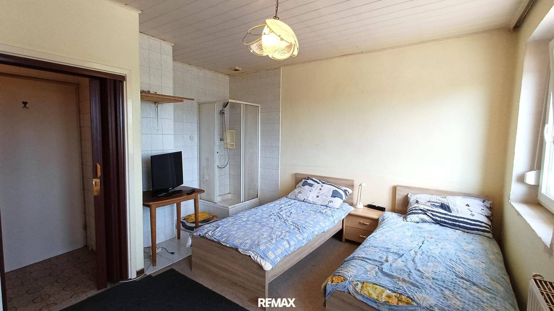 Schlafzimmer mit zwei Einzelbetten, Fernseher und integriertem Duschbereich.
