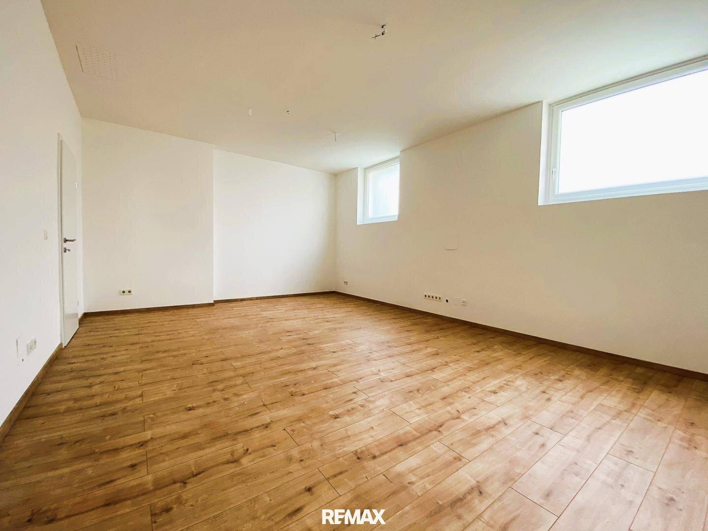 Leerer Raum mit hellen Holzdielen und weißen Wänden, der viel natürliches Licht durch zwei Fenster erhält.