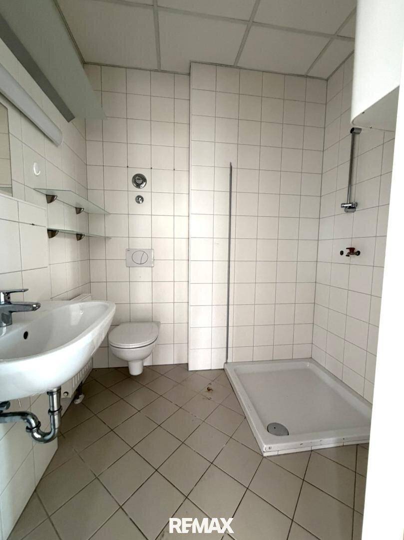 Einfaches Badezimmer mit Dusche, WC und Waschbecken, komplett gefliest.