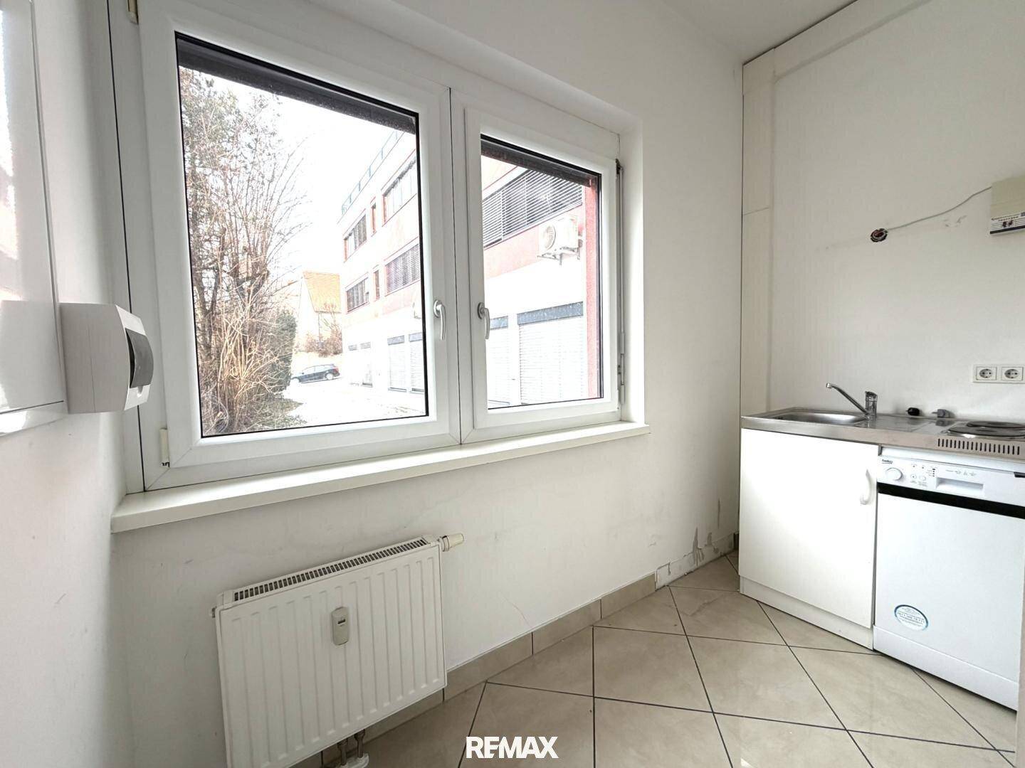 Kleine Küchenzeile mit Spüle, Kochfeld und Kühlschrank unter einem Fenster.