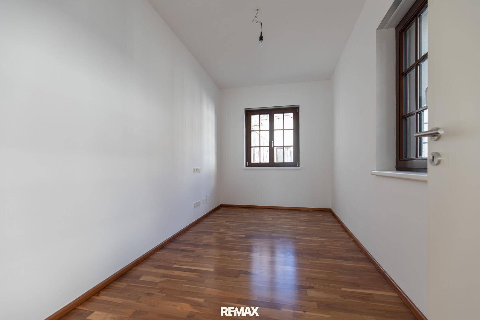 Leeres Zimmer mit Parkettboden und zwei Fenstern, ideal als Schlafzimmer oder Büro.