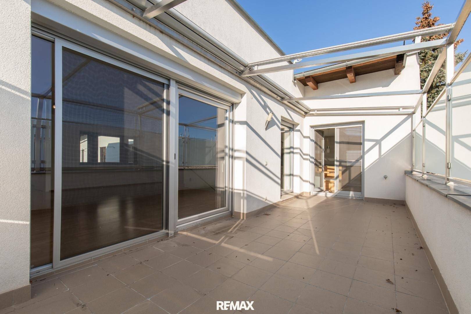 Geräumige Dachterrasse mit Fliesenboden, Glasgeländer und viel Sonnenlicht.