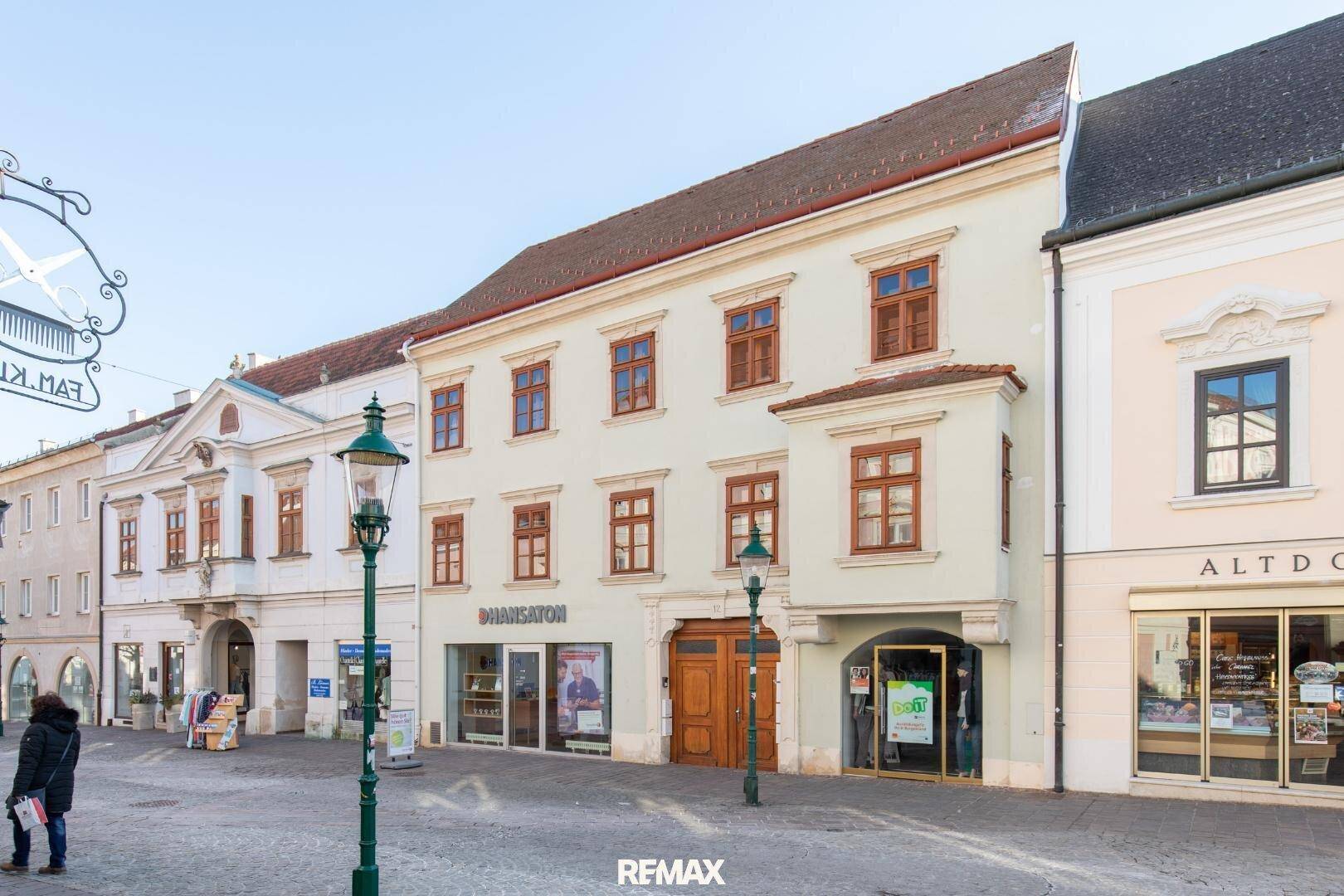Historisches Gebäude mit klassischer Fassade, vielen Fenstern und Geschäften im Erdgeschoss.