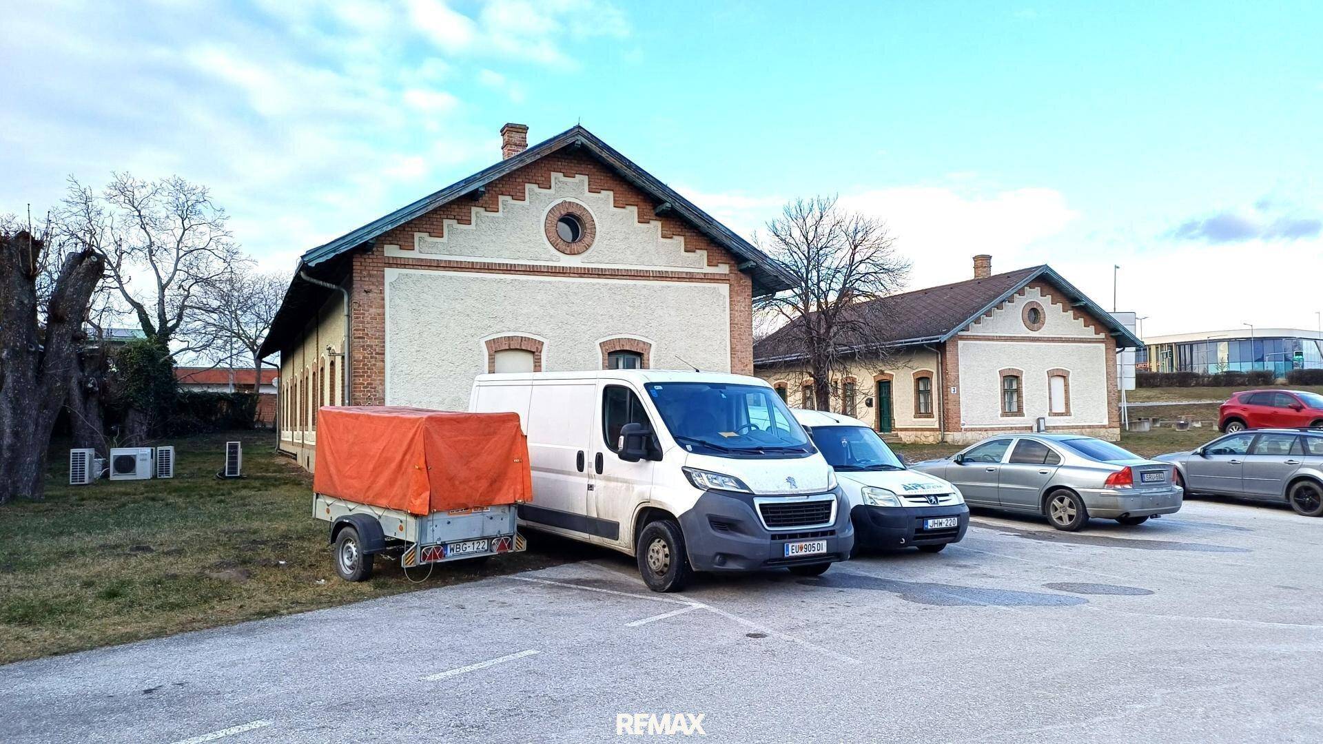 Ältere Gebäude mit Ziegeldach und Parkplätzen auf einem verschneiten Gelände.