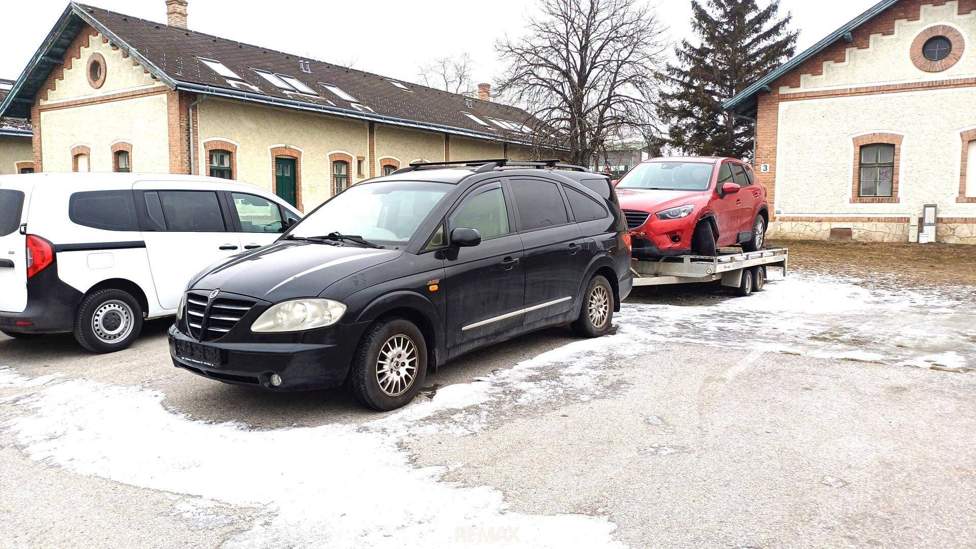 Außenansicht der älteren Gebäude mit mehreren geparkten Fahrzeugen und einem Anhänger.