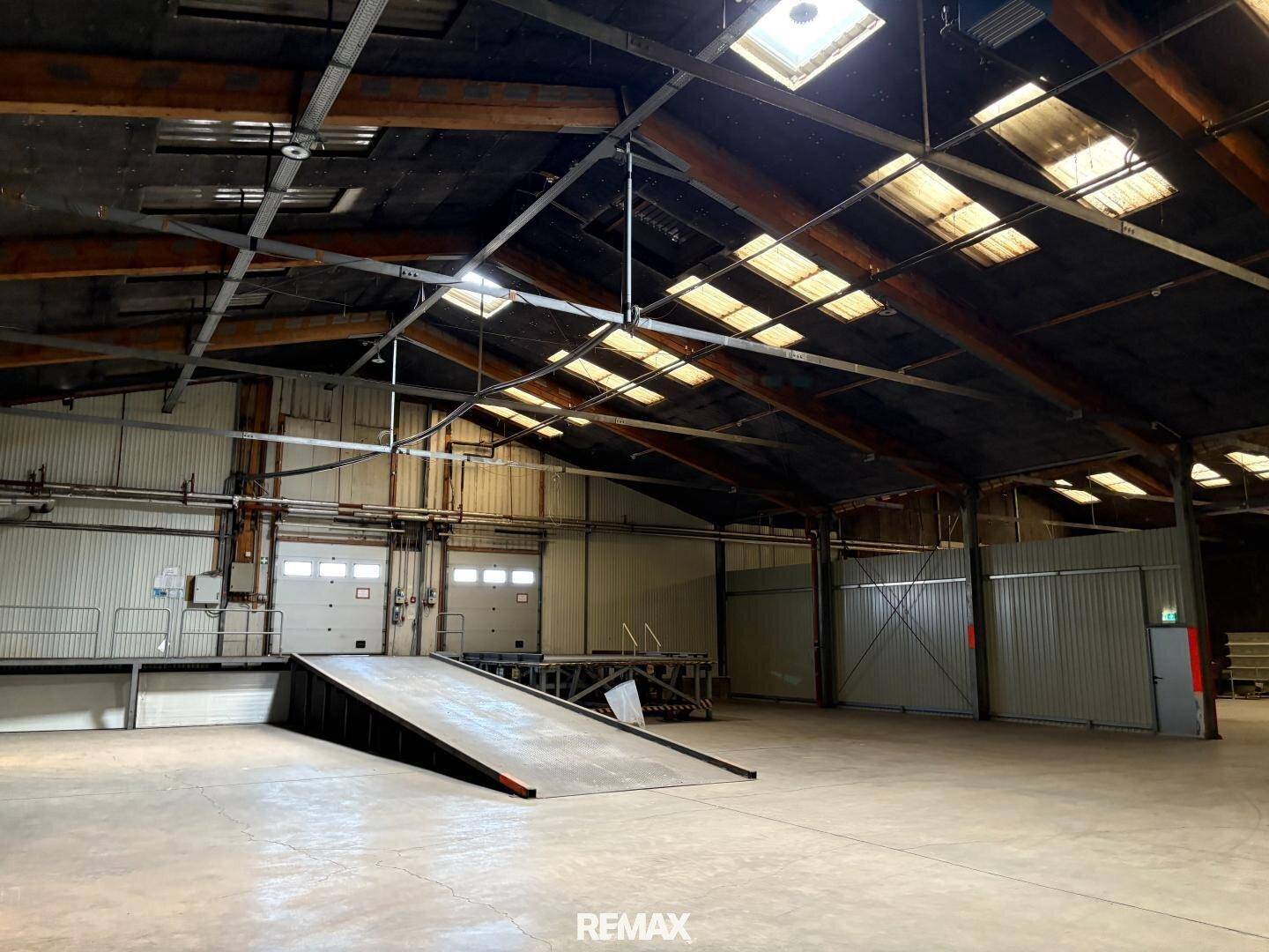 Innenansicht einer Lagerhalle mit Laderampen, Rolltoren und Oberlichtern, die natürliches Licht hereinlassen.