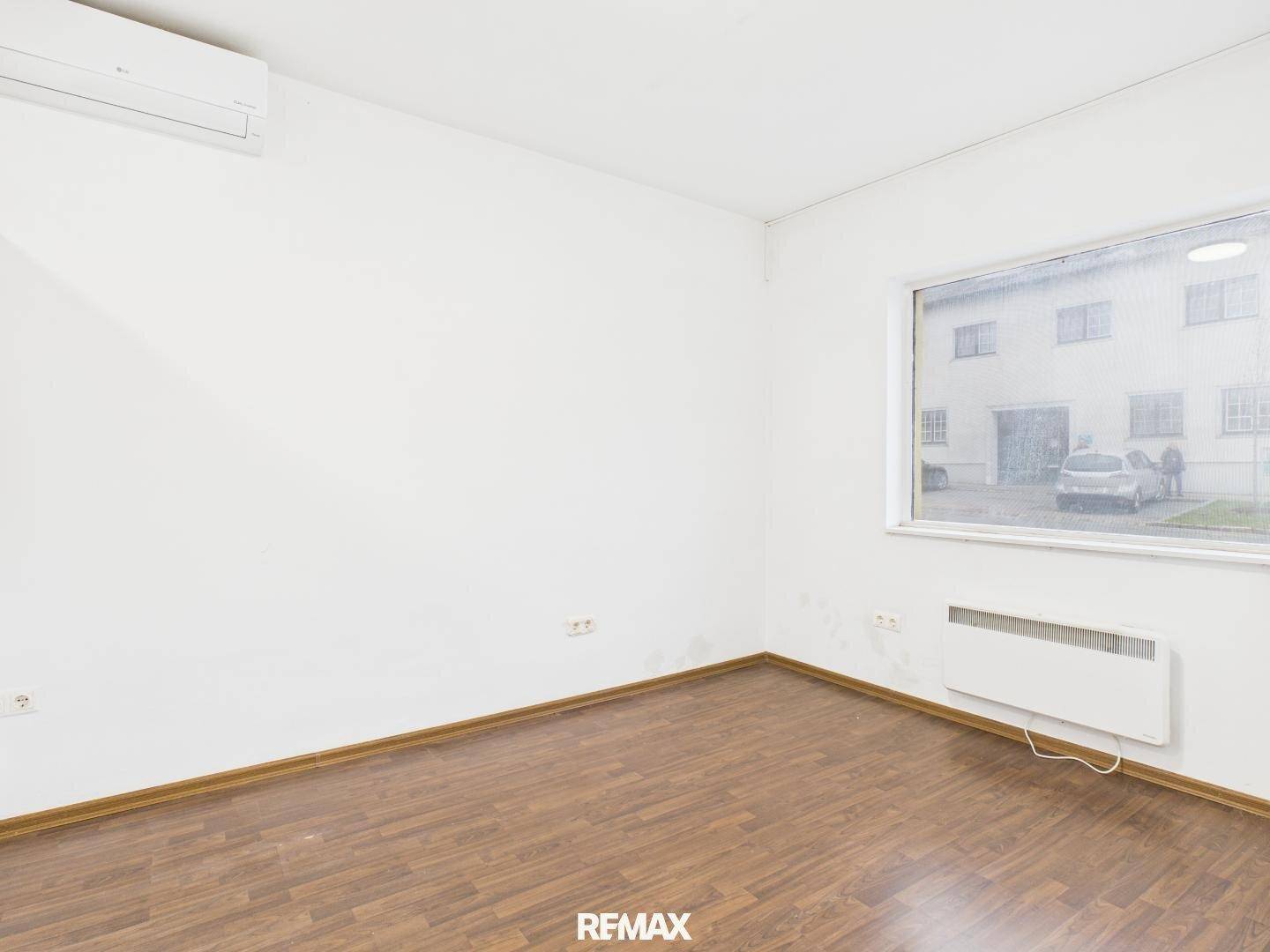 Geräumiger Büroraum mit Laminatboden, weißen Wänden und einem großen Fenster mit Blick nach draußen.
