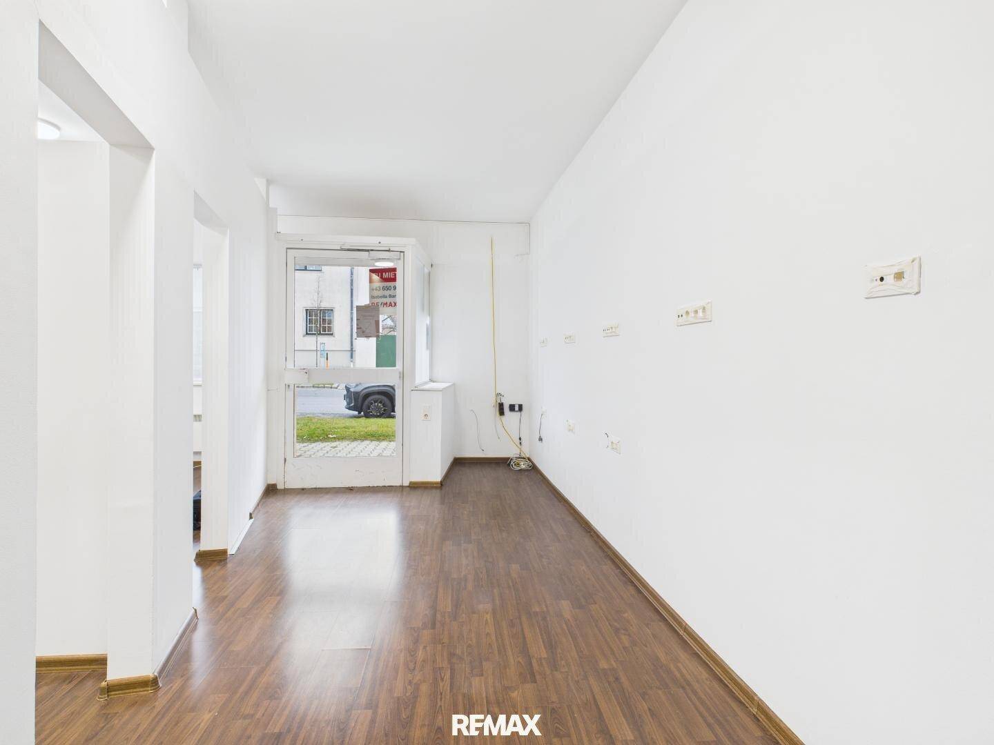 Heller Eingangsbereich mit Laminatboden und einer Glastür, die zur Straße führt, ideal für ein Geschäft.