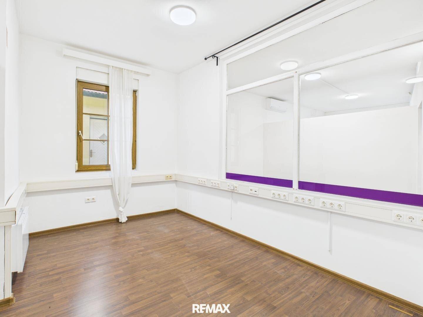 Büroraum mit Laminatboden, einem Fenster und einer internen Glaswand, die für eine helle Atmosphäre sorgt.