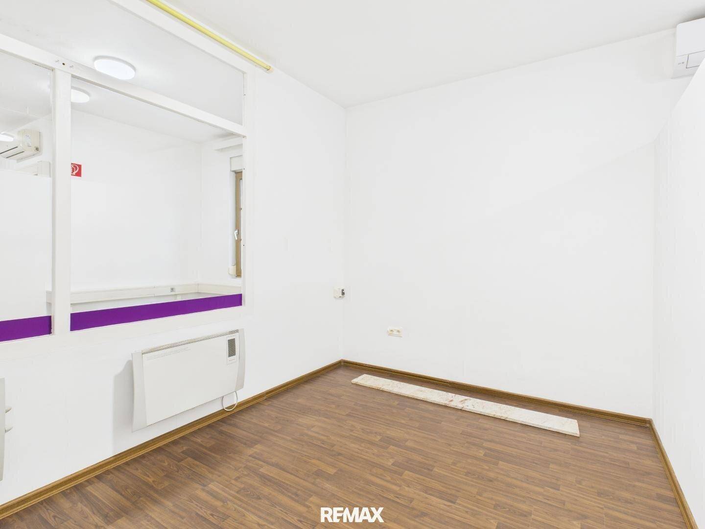 Heller Büroraum mit Laminatboden und einer internen Glaswand, die eine flexible Raumnutzung ermöglicht.