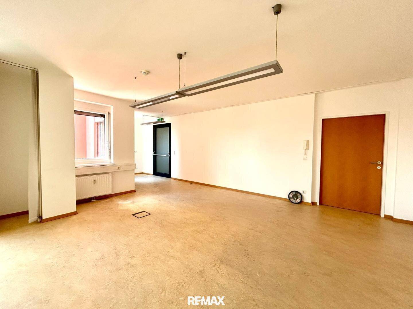 Leeres Büro mit hellem Boden, weißen Wänden und einer dunklen Tür, bereit zur individuellen Gestaltung.