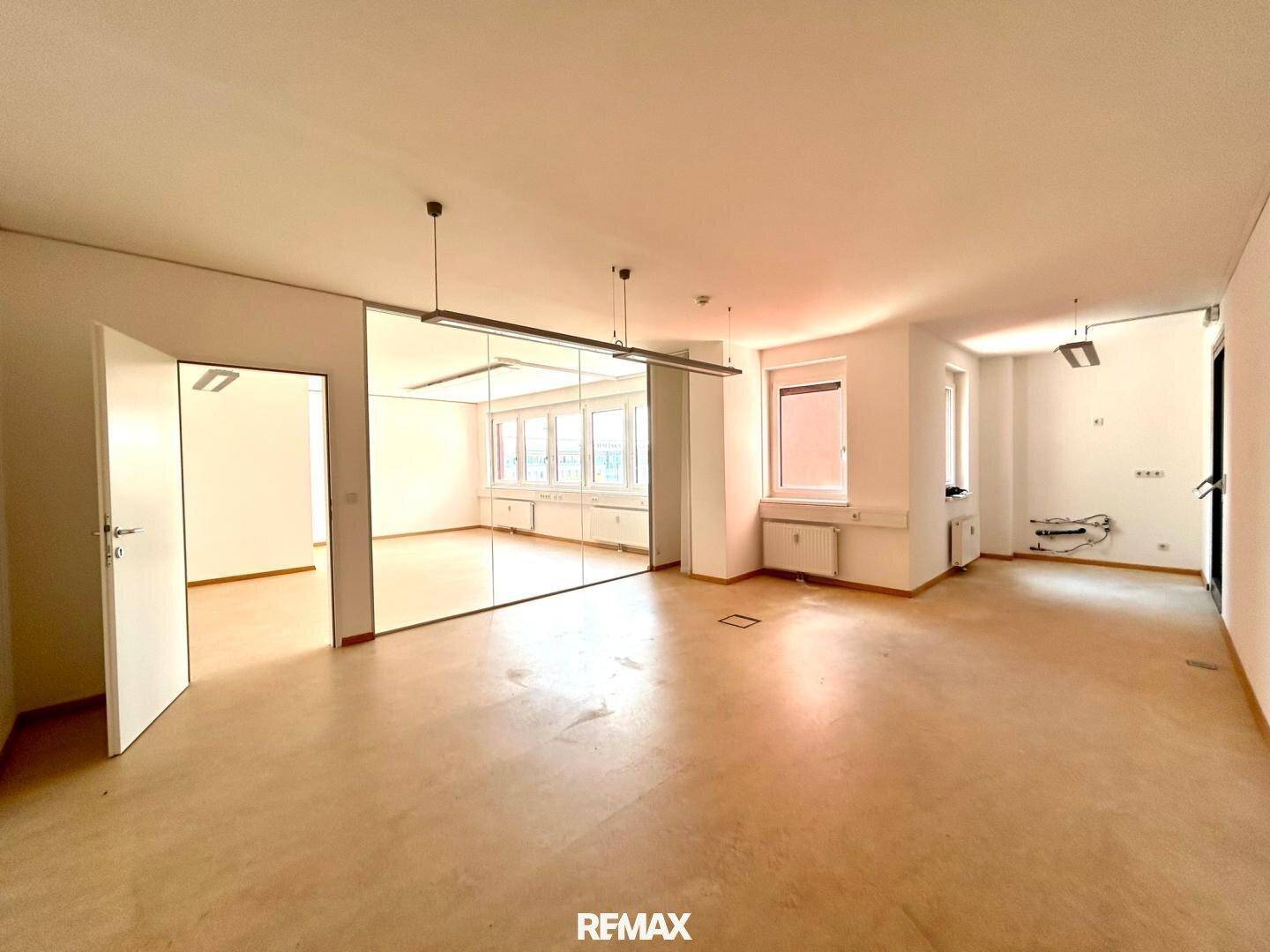 Geräumiges Büro mit heller Einrichtung, großen Fenstern und einer modernen Glaswand für flexible Raumgestaltung.