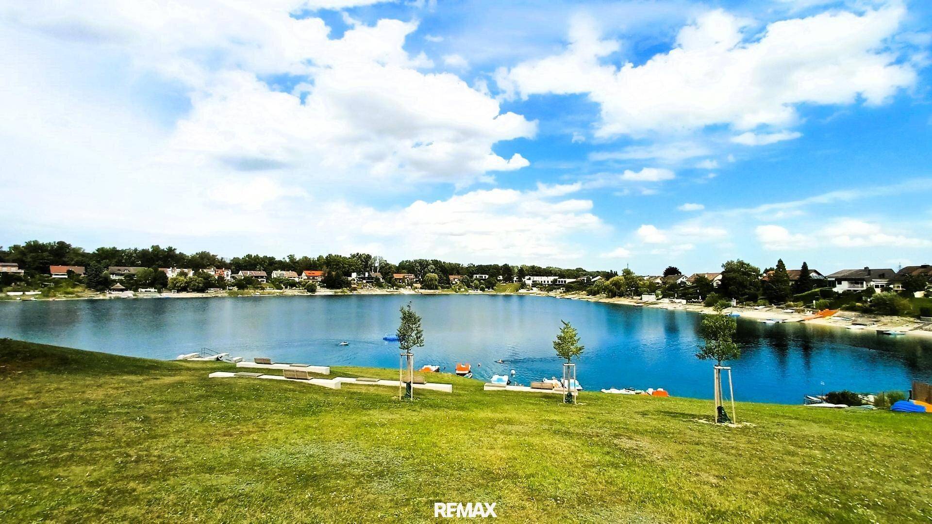 Malerischer Blick auf einen blauen See mit grünen Ufern und einem klaren Himmel mit weißen Wolken.