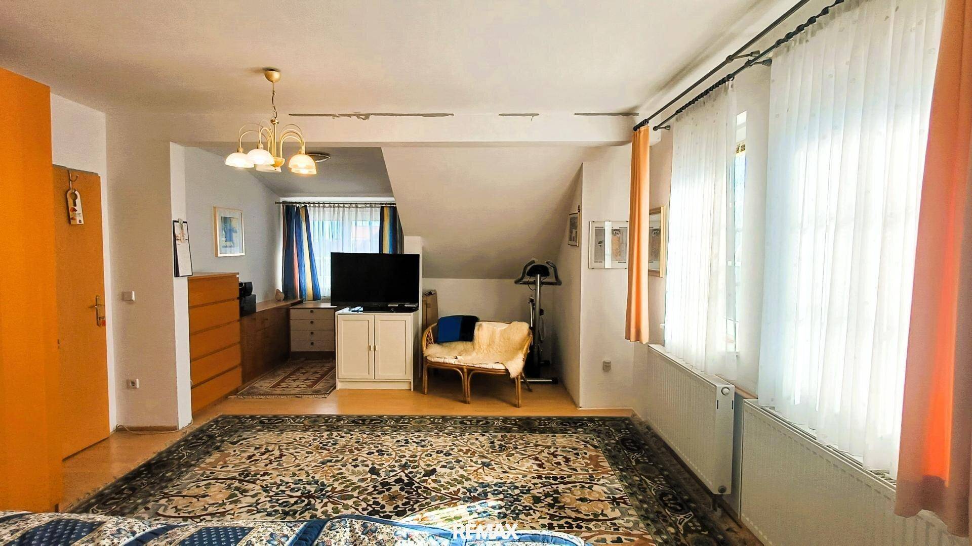 Geräumiges Schlafzimmer im Dachgeschoss mit großen Fenstern, Teppichboden und schrägen Wänden.