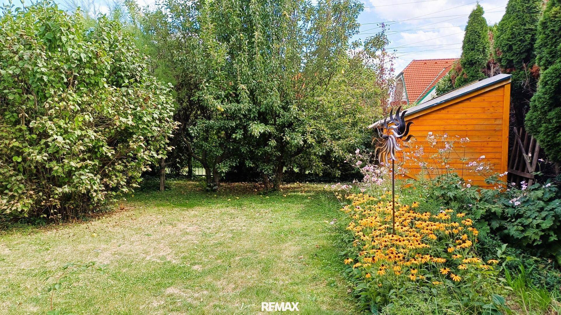 Weiterer Teil des Gartens mit Rasenfläche, Blumen und einem kleinen Holzschuppen im Hintergrund.