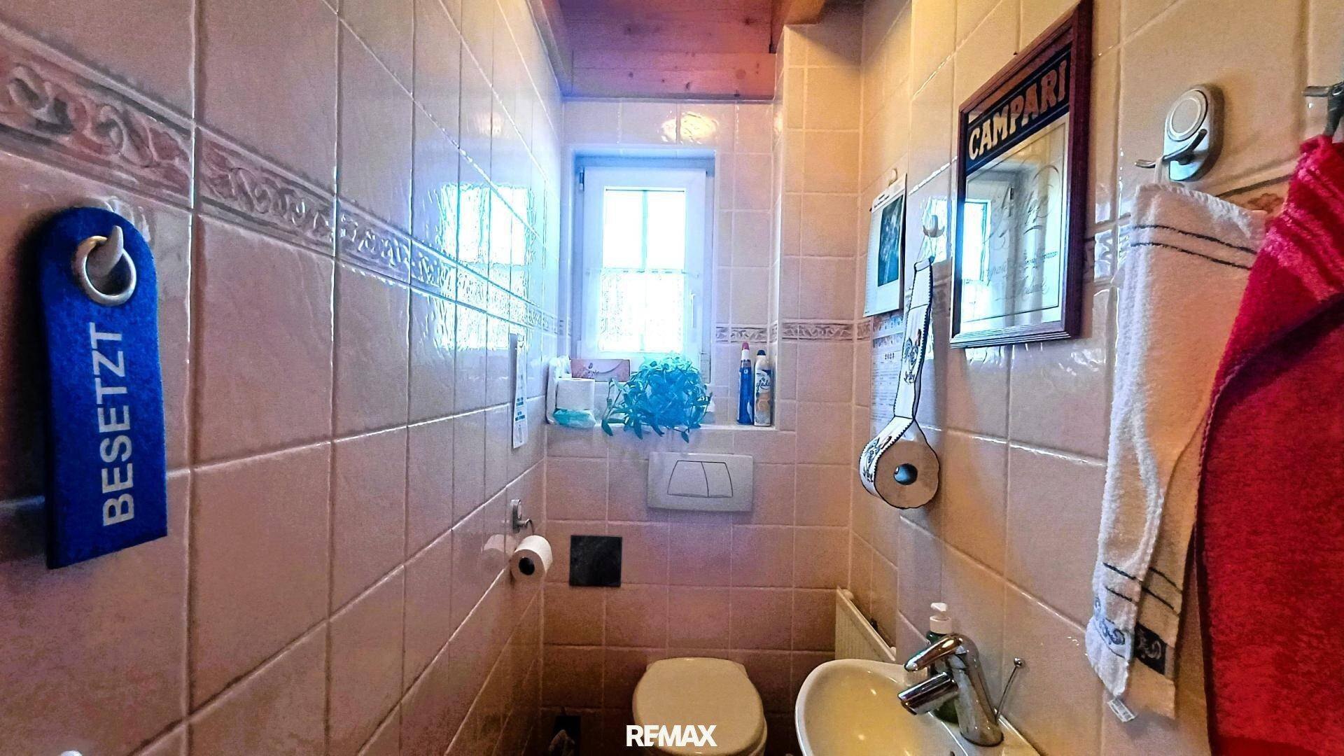 Kleines Gäste-WC mit beigen Fliesen, Fenster und einem Waschbecken, unter einer Holzdecke.