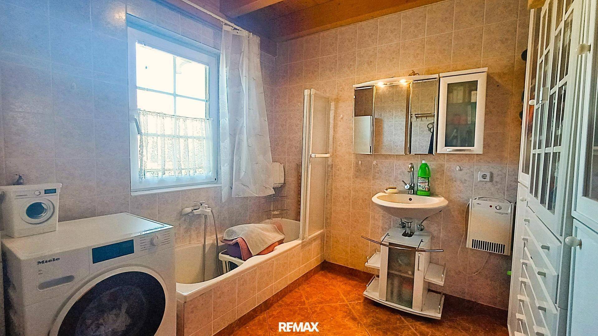 Badezimmer mit Fliesen, Badewanne, Dusche und Waschmaschine, unter einer Holzdecke.