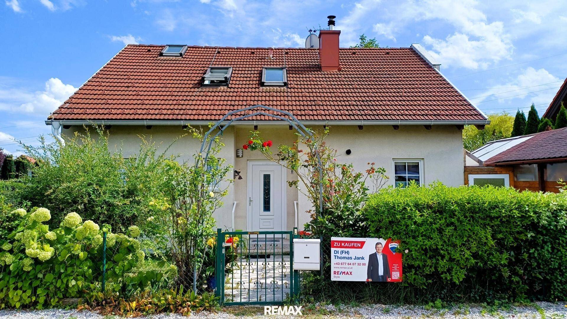 Vorderansicht eines Einfamilienhauses mit rotem Ziegeldach, umgeben von einem gepflegten Garten und Hecken.