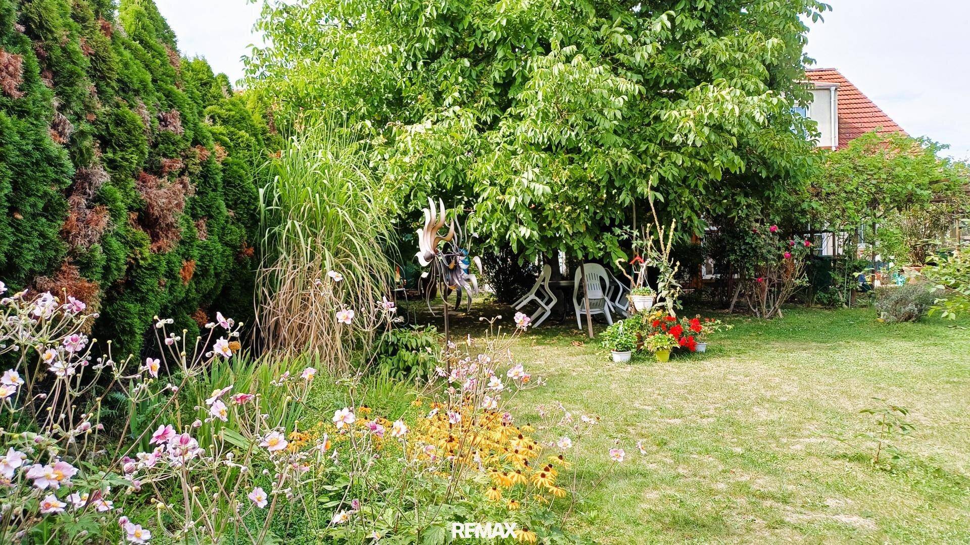 Gepflegter Gartenbereich mit Rasen, Blumenbeeten und schattenspendenden Bäumen, ideal zum Entspannen.