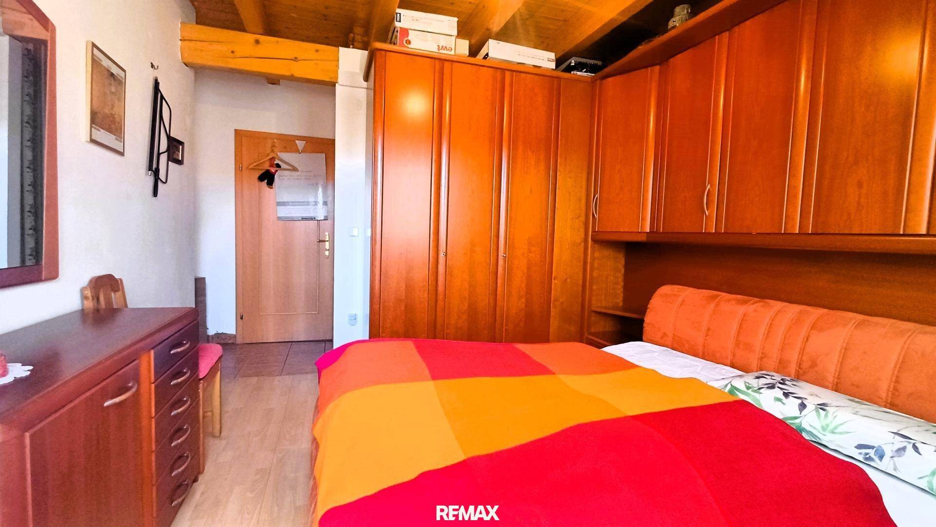 Schlafzimmer mit Holzschränken, Holzbalkendecke und einem bunten Bettüberwurf.