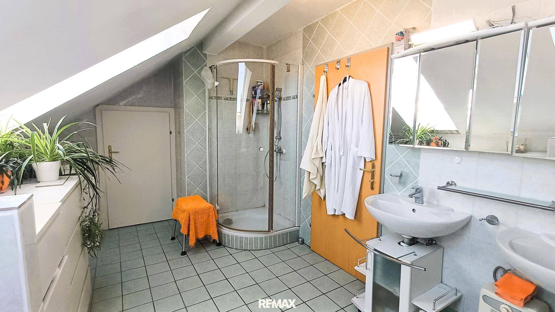 Dachgeschoss-Badezimmer mit Dusche, Waschbecken und Fliesenboden, unter einer schrägen Decke.