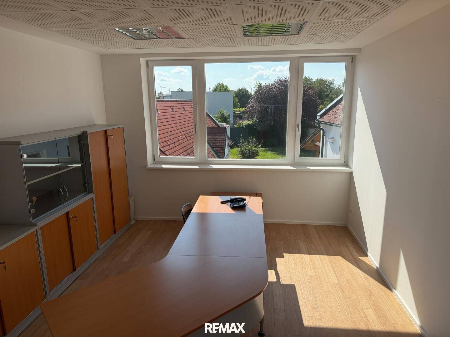 Geräumiges Büro mit Holzboden, großen Fenstern und einem langen Schreibtisch mit Stauraum.