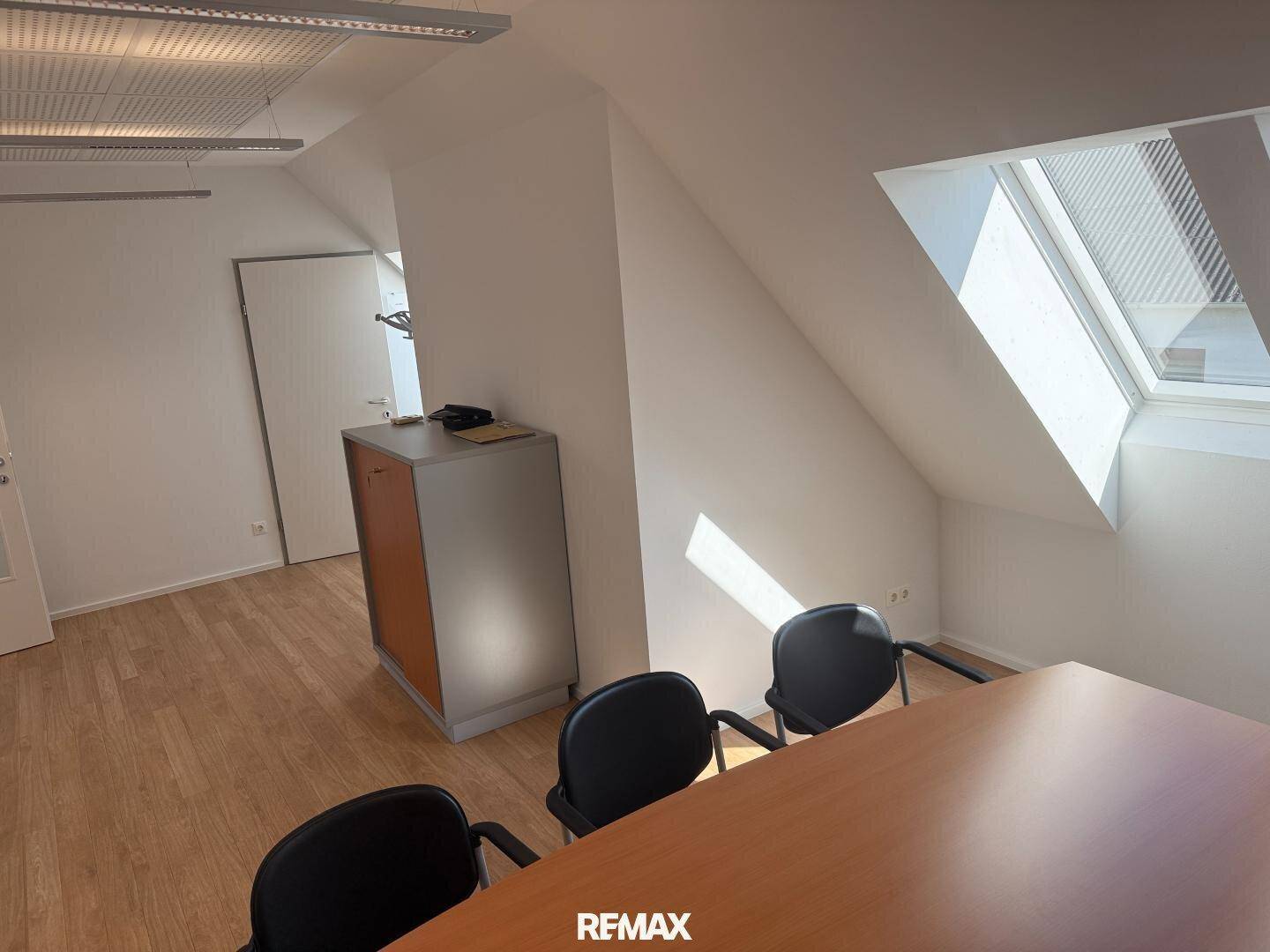 Heller Büroraum mit Dachschrägen, Holzboden und einem Schrank, der viel Stauraum bietet.
