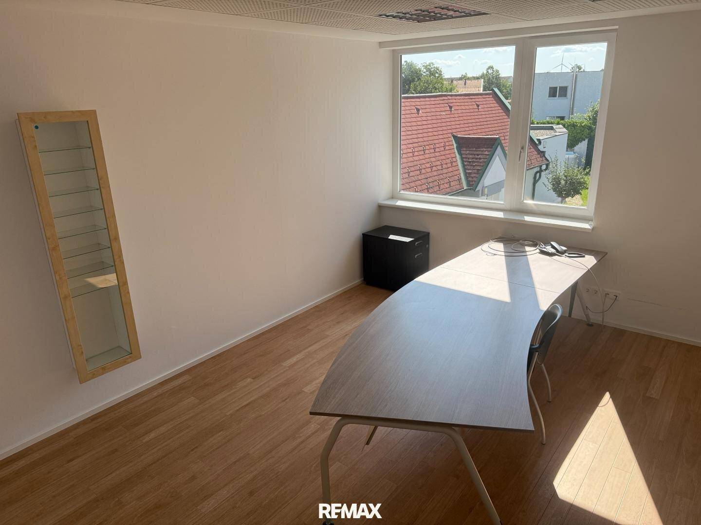 Helles Büro mit Holzboden, großem Fenster und einem geschwungenen Schreibtisch.