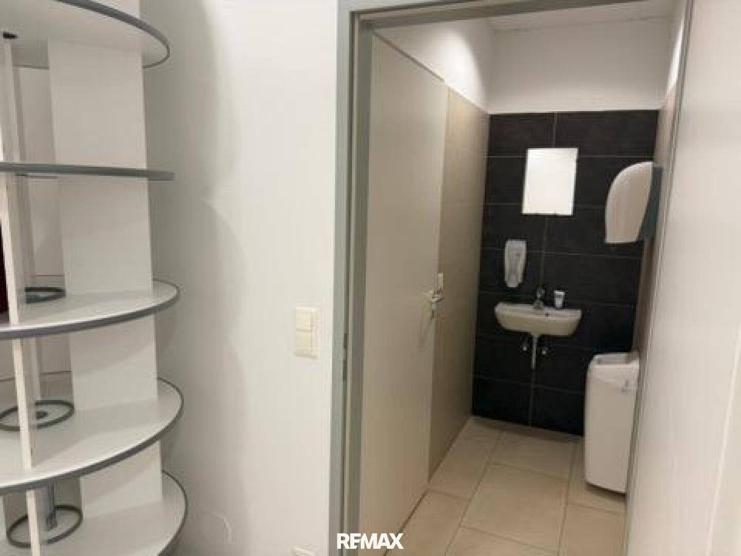 Moderne Gästetoilette mit dunklen Fliesen, kleinem Waschbecken und Handtuchspender.