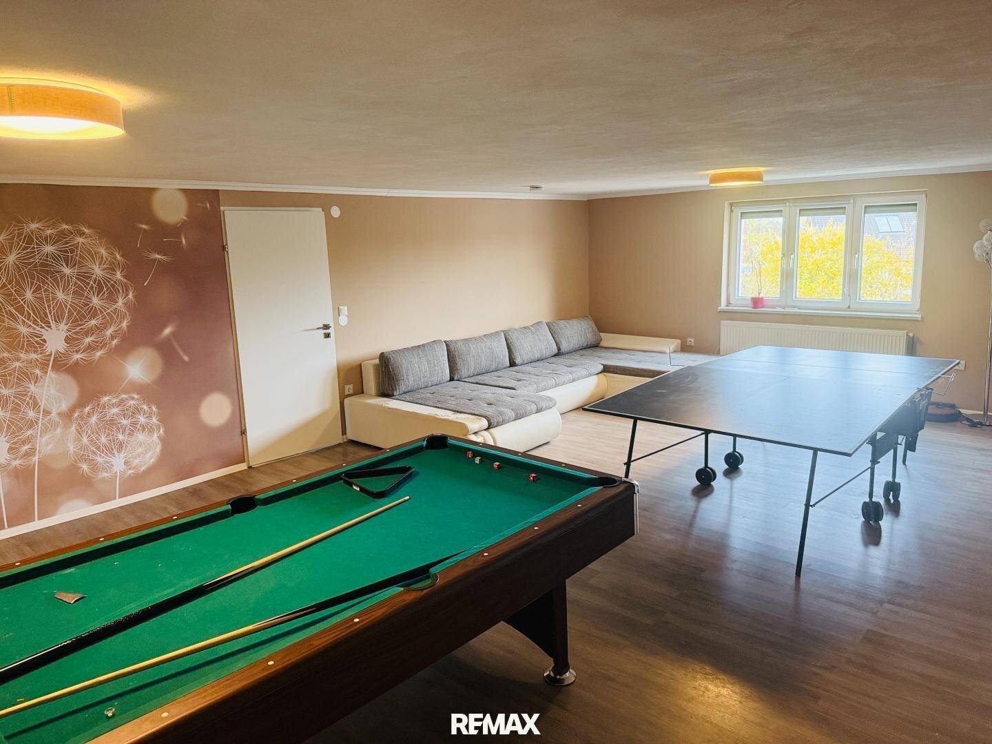 Geräumiger Freizeitraum mit Billardtisch, Tischtennisplatte und großem Sofa.