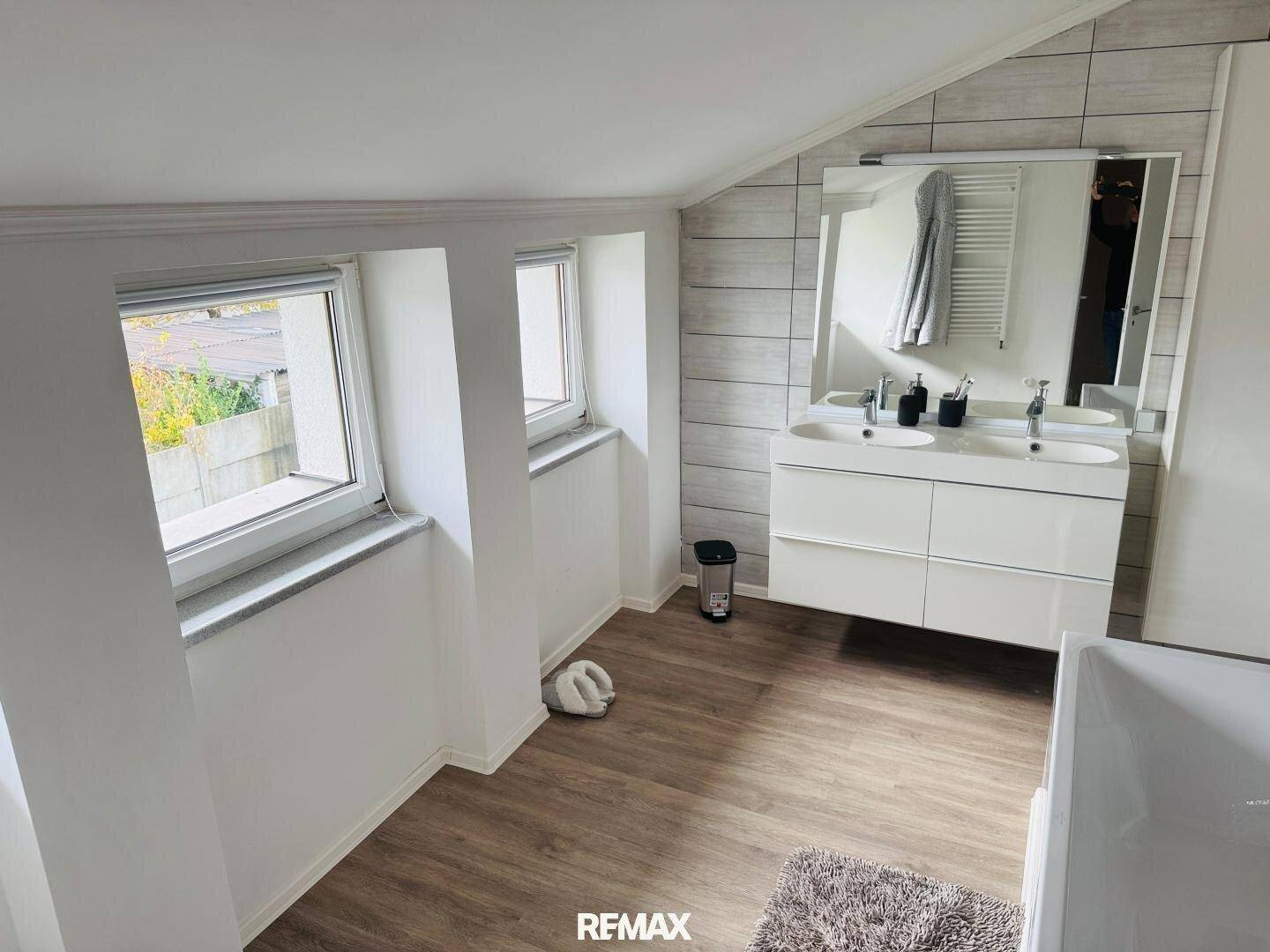 Helles Badezimmer mit Doppelwaschbecken, Spiegel und Fenstern unter der Dachschräge.