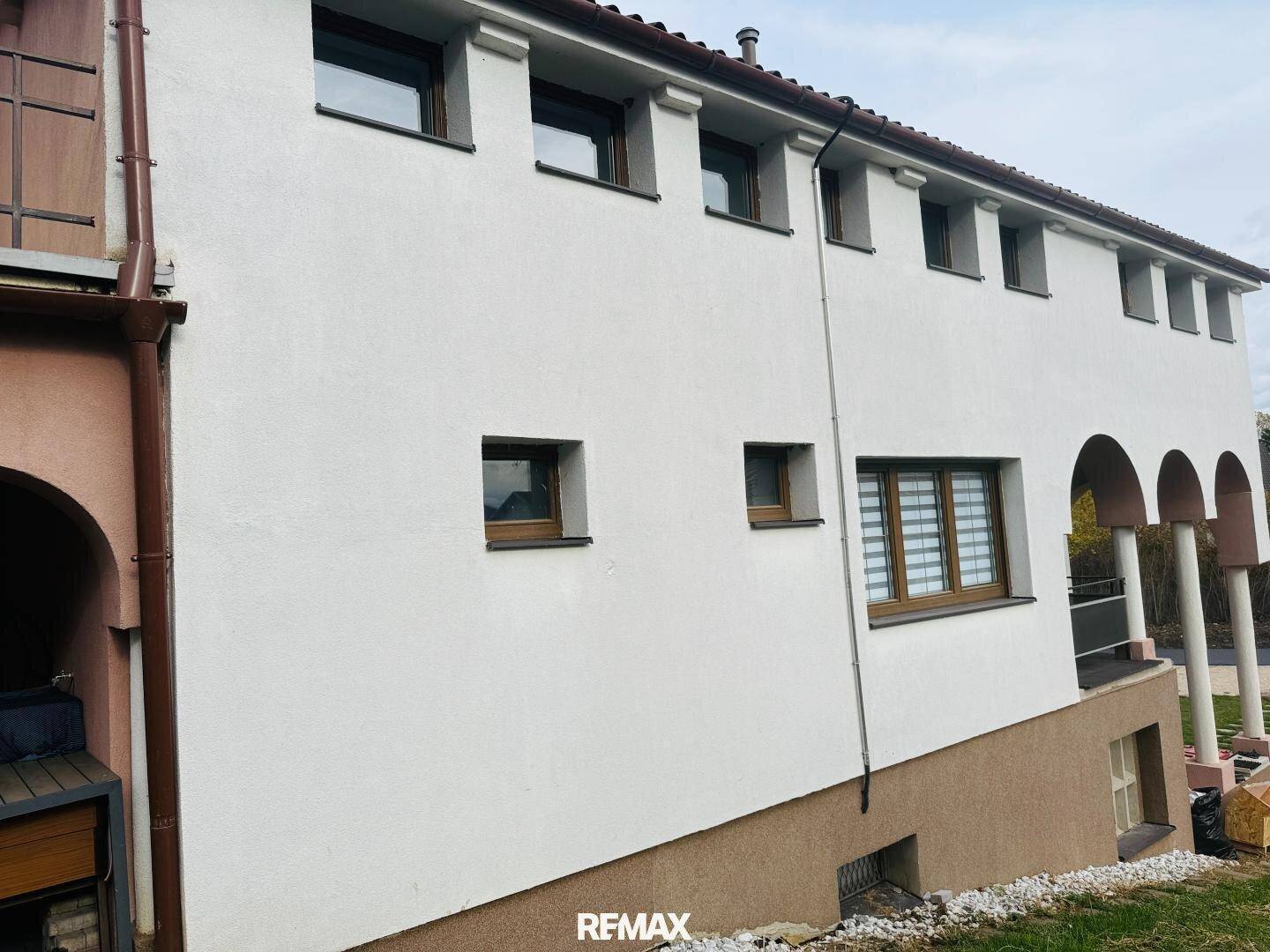 Seitenansicht des Hauses mit weißer Fassade, braunem Sockel und mehreren Fenstern.