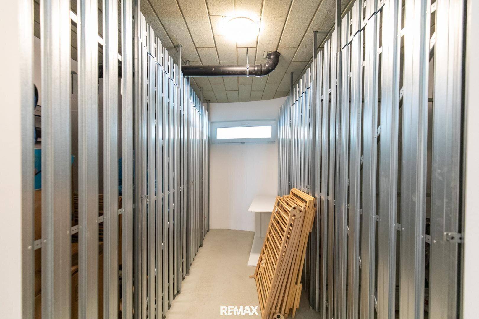 Praktischer Abstellraum im Keller mit Metallabtrennungen und kleinem Fenster.