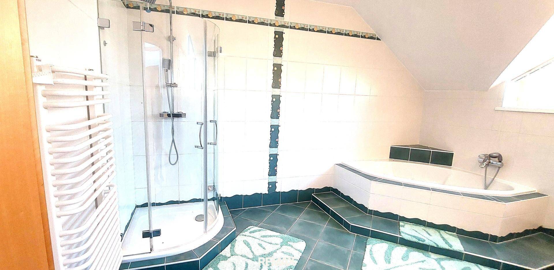 Badezimmer mit Eckdusche, Eckbadewanne, grünen Fliesen und beheiztem Handtuchhalter unter der Dachschräge.