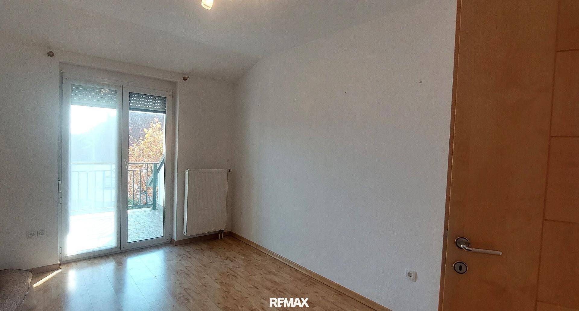 Leerer Raum mit Holzboden und Glasschiebetüren, die Zugang zu einem Balkon bieten.
