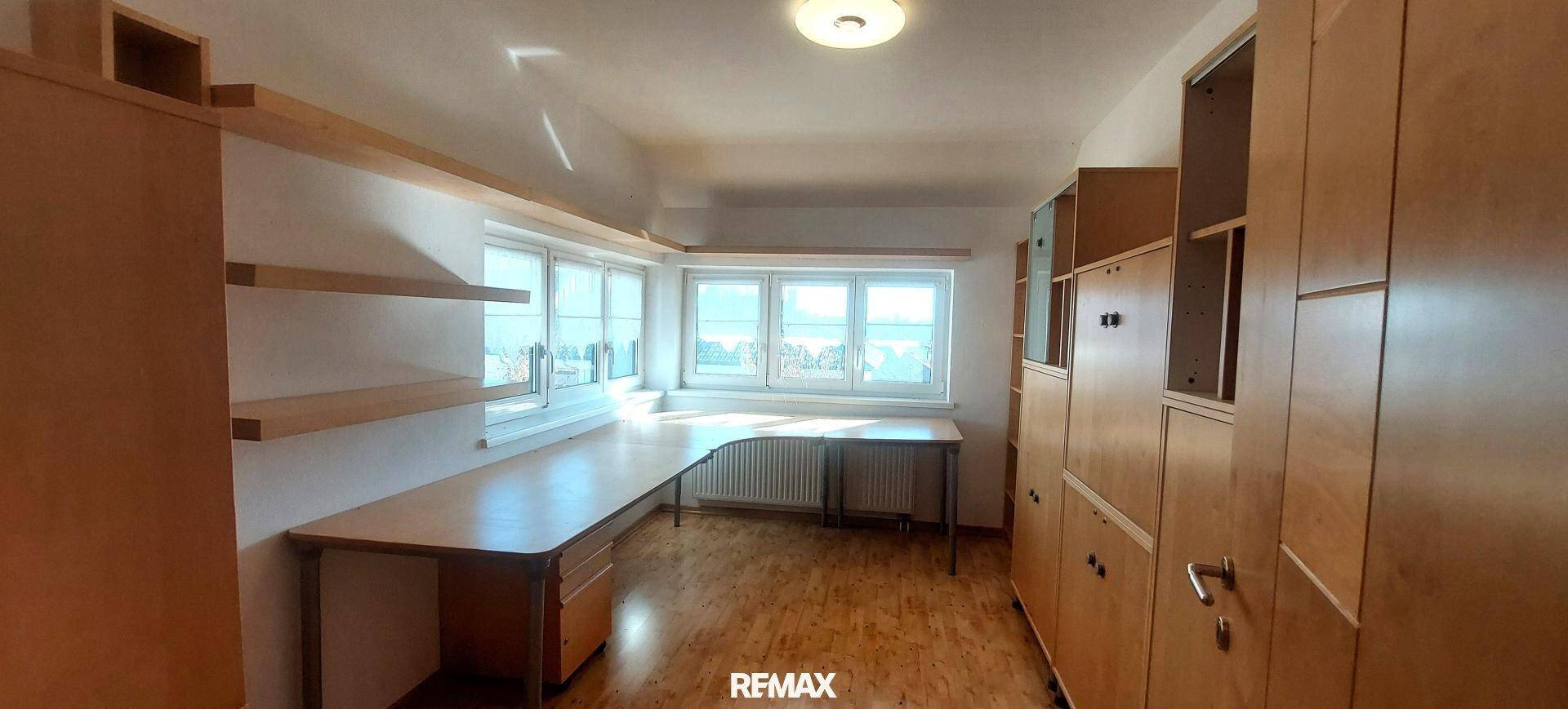 Geräumiges Arbeitszimmer mit langem Holzschreibtisch, Einbauregalen und mehreren Fenstern.