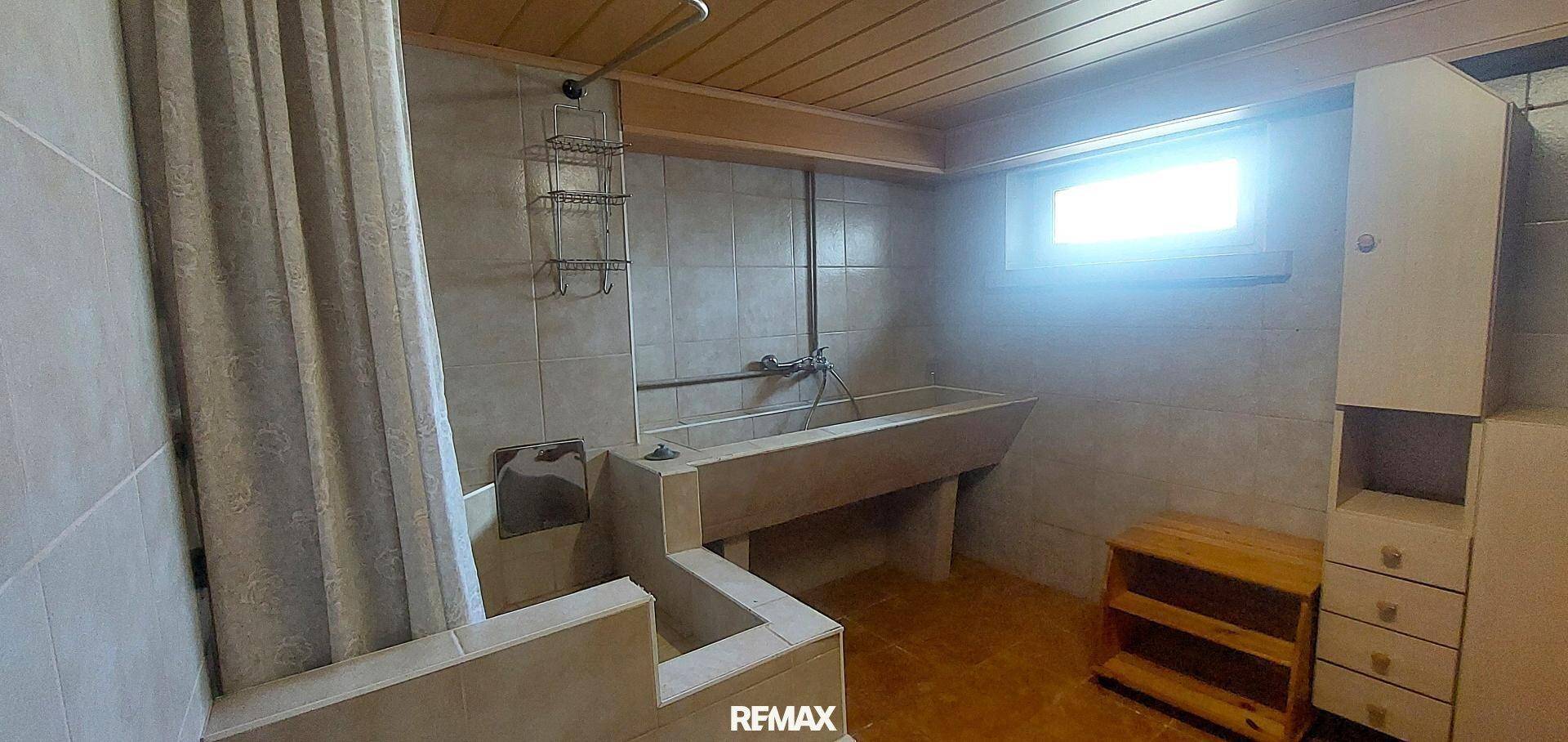 Funktionales Badezimmer im Keller mit Duschbereich, großem Waschbecken und Holzdecke.