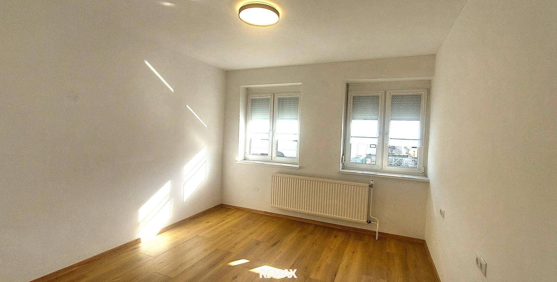 Heller, leerer Raum mit Holzboden und zwei Fenstern, bereit zur individuellen Gestaltung.