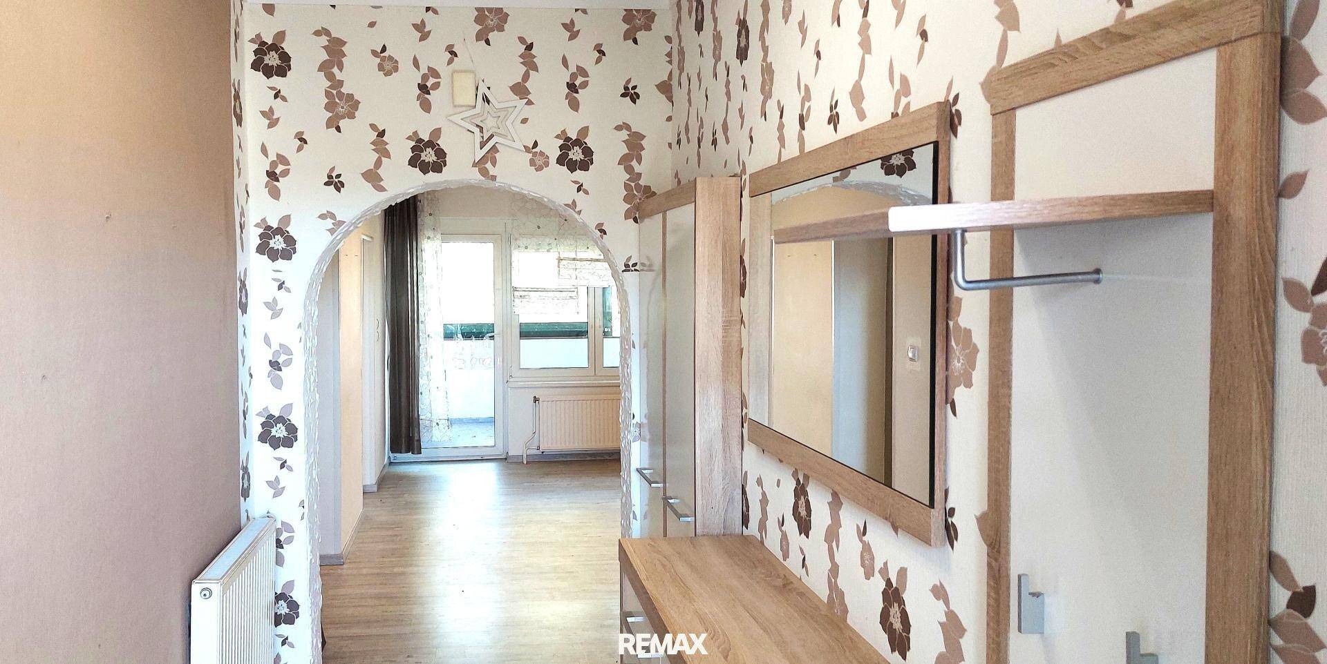 Flur mit floraler Tapete, Spiegel und Zugang zu einem hellen Raum mit Balkon.